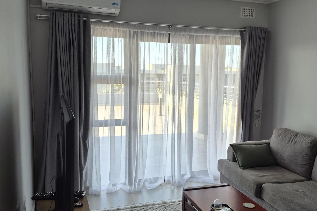 A bright living room featuring large sliding glass doors leading to a balcony, equipped with a wall-mounted air conditioning unit and recessed ceiling lighting.