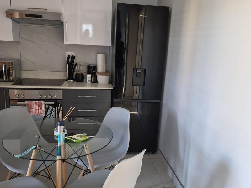 Modern open-plan kitchen featuring sleek white and grey cabinetry, integrated stainless steel oven, extractor fan, and tiled flooring.