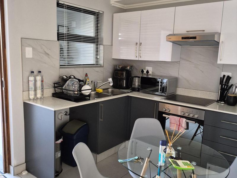 Modern open-plan kitchen featuring two-tone cabinetry, stone-look splashbacks, integrated oven, hob, and extractor fan, seamlessly flowing into the dining area.