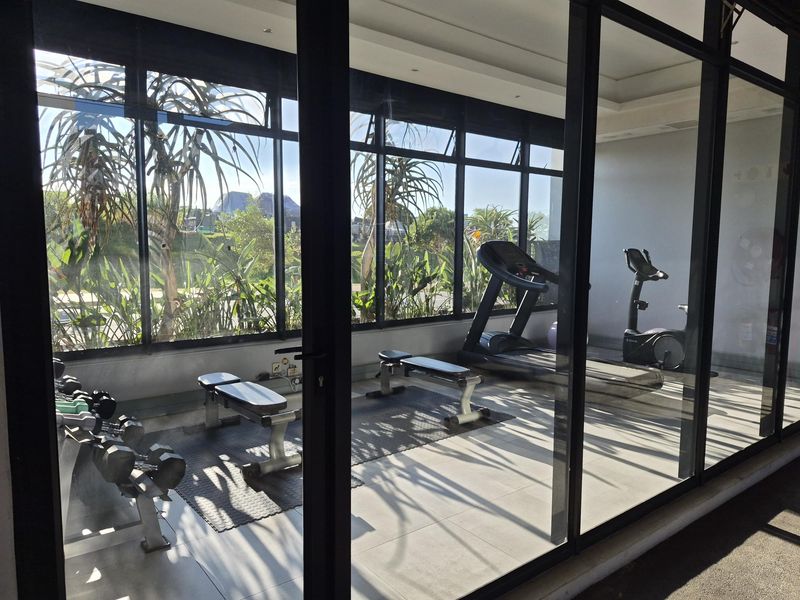 A well-lit gym facility featuring large floor-to-ceiling windows, tiled flooring, and a modern glass-enclosed design.