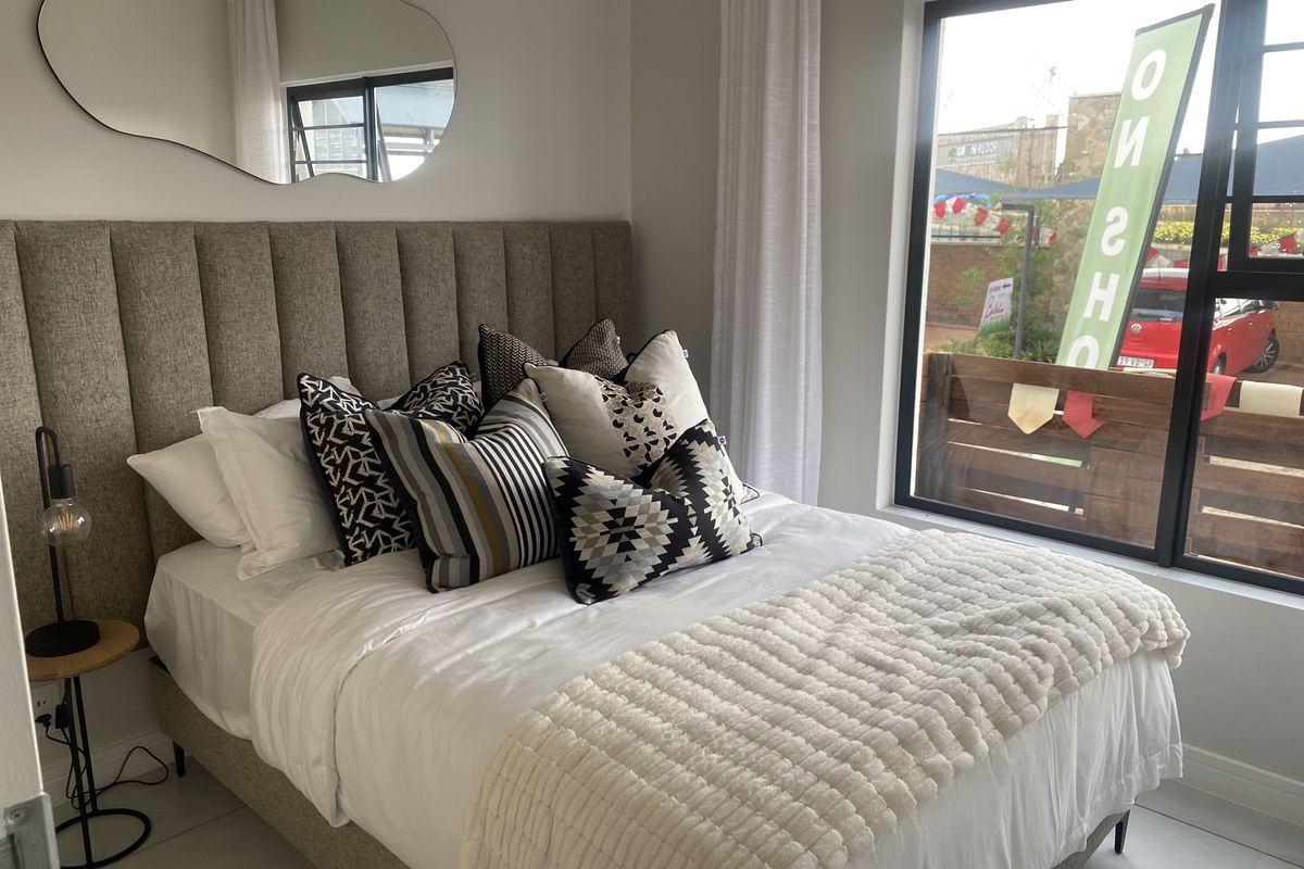 A well-lit bedroom featuring a large window, neutral wall finishes, and a modern upholstered headboard.