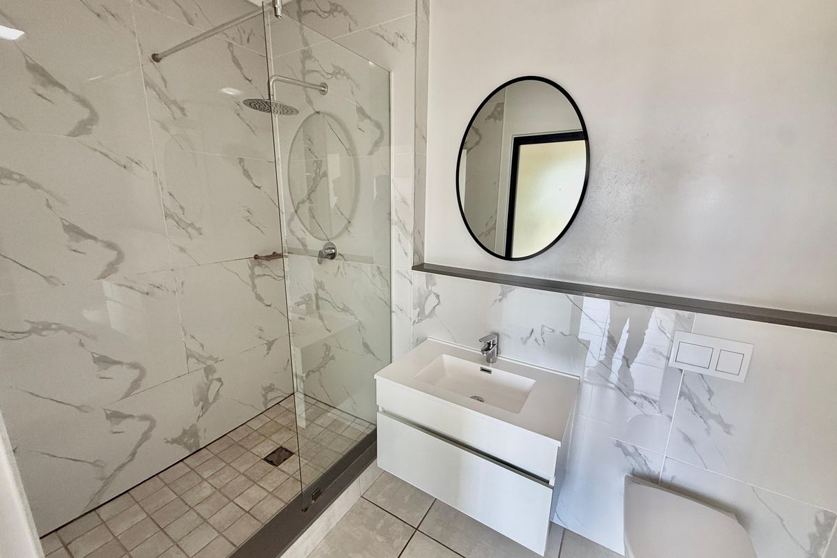 Modern bathroom featuring a walk-in shower with glass enclosure, marble-look wall tiles, wall-mounted vanity, and a contemporary toilet.