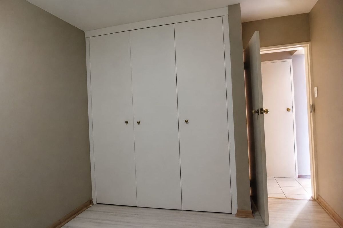 A vacant bedroom featuring light-toned laminate flooring and a white built-in wardrobe with a doorway leading to an adjacent room.