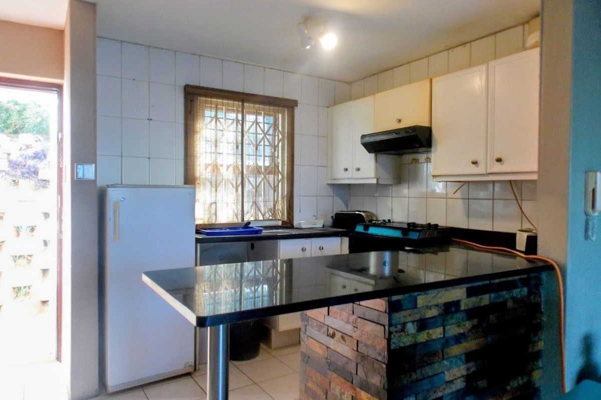 Functional kitchen featuring granite countertops, a breakfast bar, built-in cabinetry, and a tiled backsplash with direct access to the exterior.