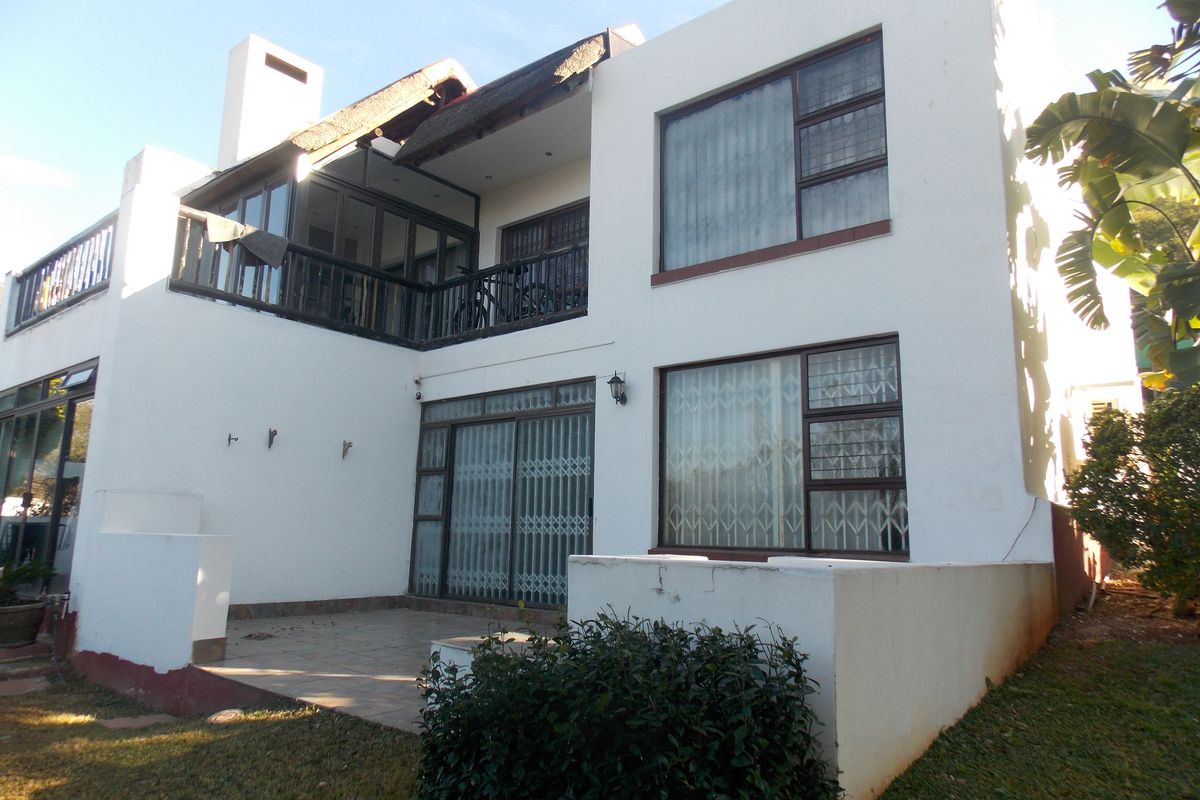 Rear view of a two-story townhouse featuring a tiled patio, balcony, sliding glass doors with security gates, and a thatched roof section.