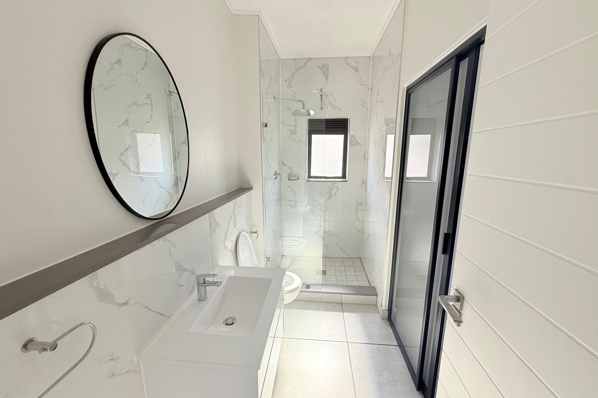 Modern bathroom featuring marble-look wall tiles, a sleek vanity with basin, a glass-enclosed walk-in shower, and contemporary black fixtures.