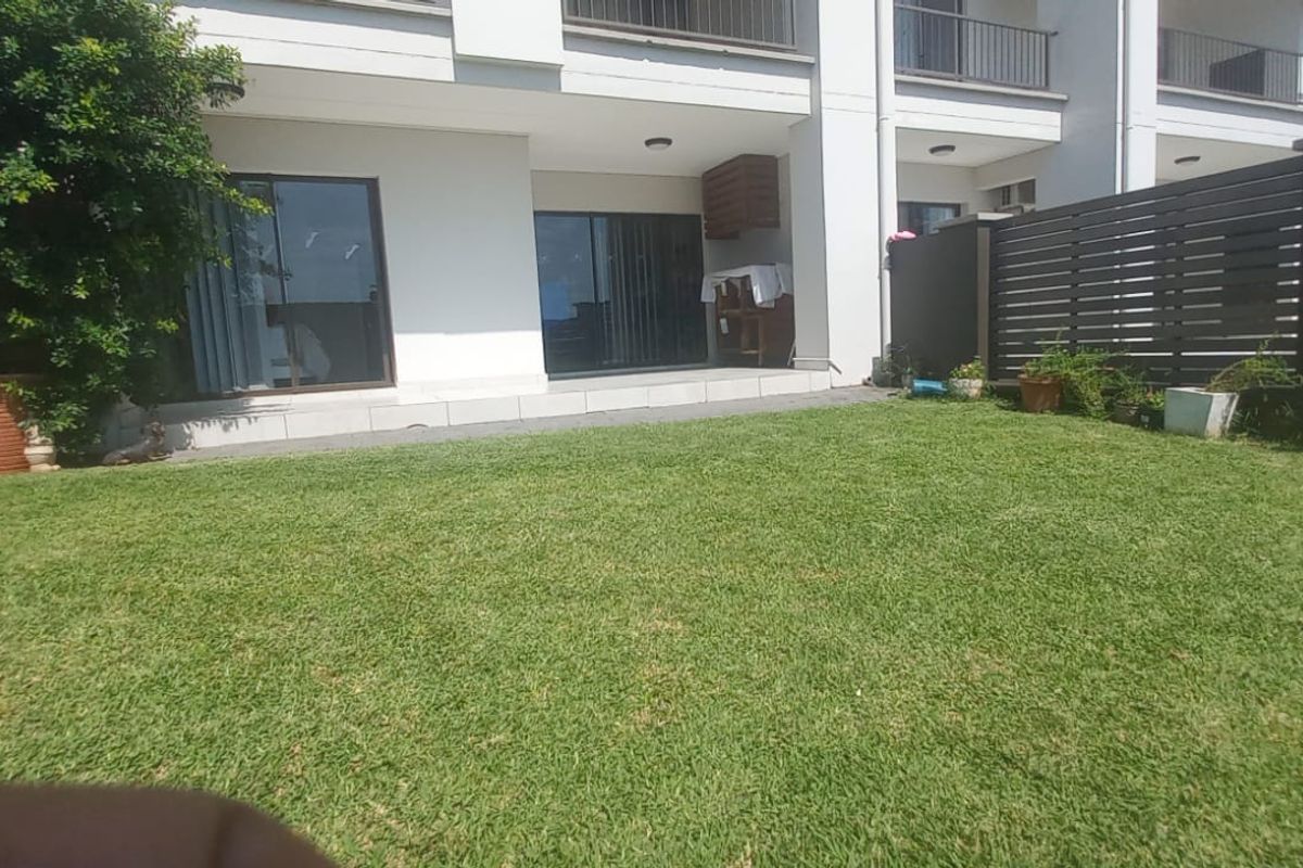 A private rear garden featuring a well-maintained lawn, paved patio area, and perimeter fencing, providing a pleasant outdoor space for the apartment.
