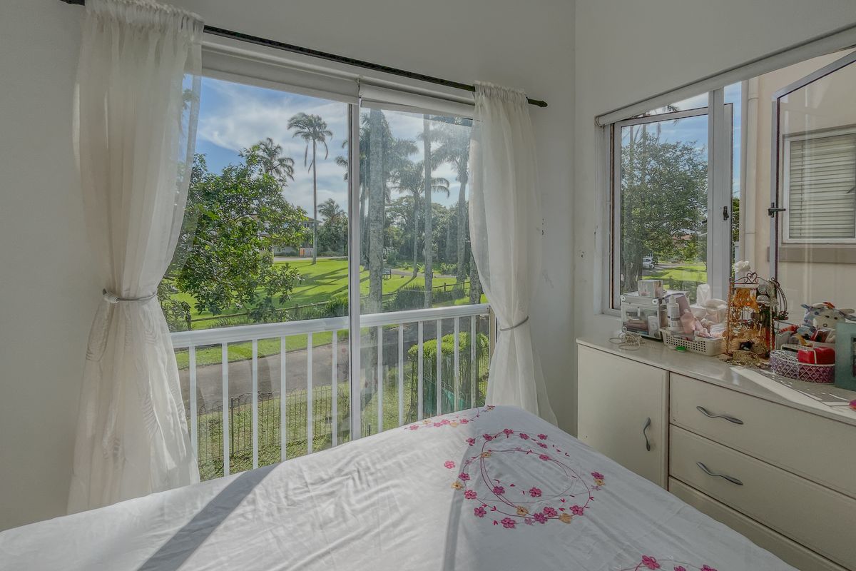 A bright bedroom featuring large sliding glass doors that open to a balcony with scenic garden and estate views.