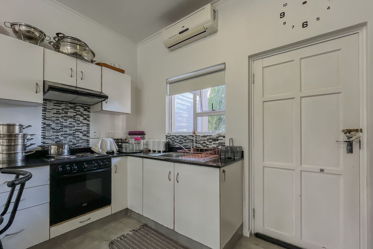 Compact kitchen featuring white cabinetry, dark granite countertops, mosaic tile backsplash, built-in oven with extractor fan, and a wall-mounted air conditioning unit.