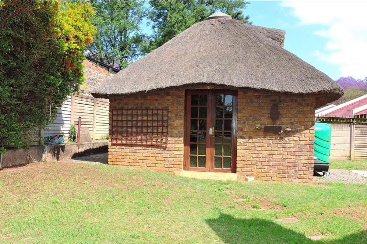 A detached garden structure featuring traditional thatch roofing, exposed brick walls, and double glass-paneled doors set within a landscaped yard.