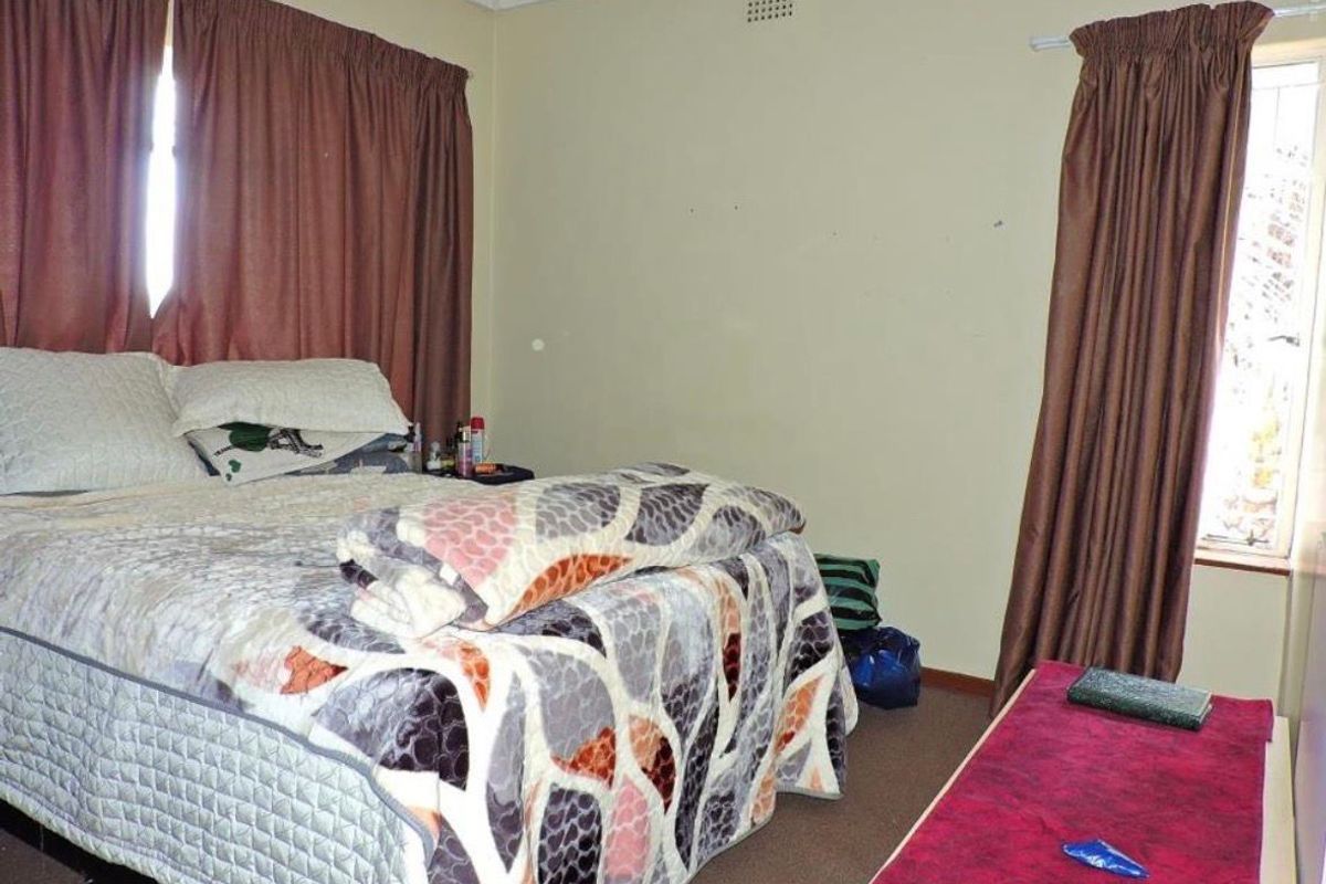 A standard bedroom featuring carpeted flooring, neutral wall finishes, and dual windows with curtain treatments.
