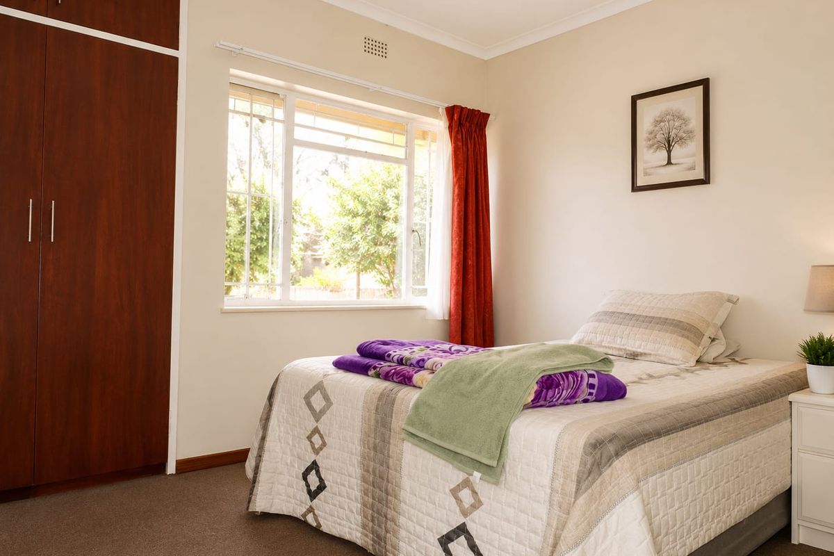 A well-lit bedroom featuring neutral walls, carpeted flooring, and a built-in wooden wardrobe with ample storage space.