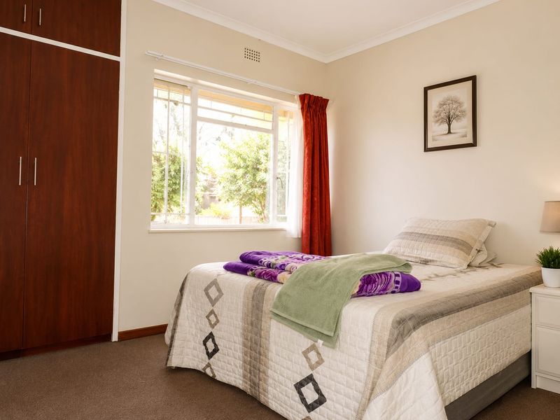 A well-lit bedroom featuring neutral walls, carpeted flooring, and a built-in wooden wardrobe with ample storage space.