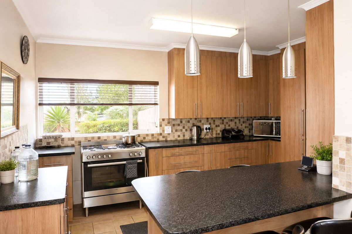 A well-maintained kitchen featuring wood-finish cabinetry, granite countertops, a stainless steel gas stove, and a tiled backsplash with modern pendant lighting.