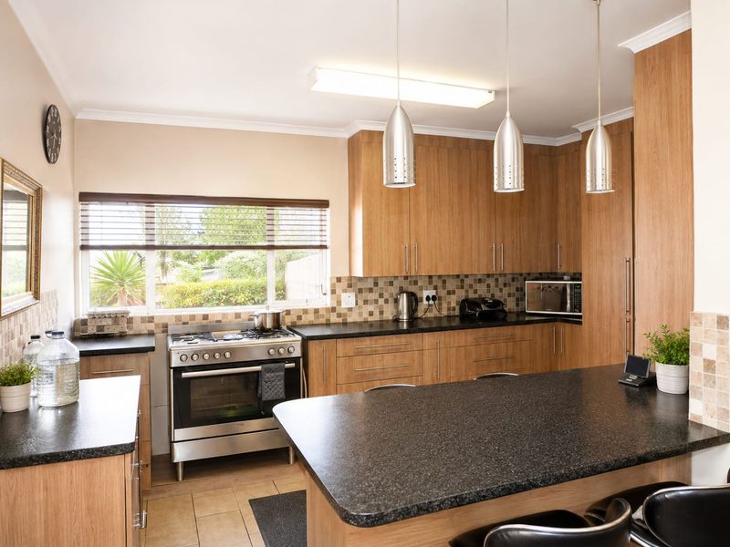 A well-maintained kitchen featuring wood-finish cabinetry, granite countertops, a stainless steel gas stove, and a tiled backsplash with modern pendant lighting.