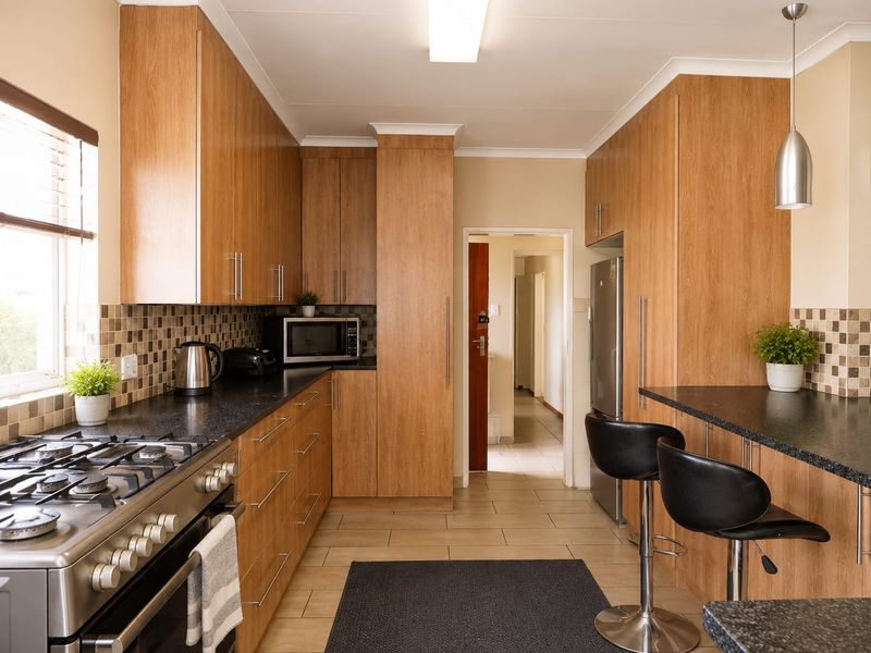 Modern kitchen featuring wood-finish cabinetry, granite countertops, a gas stove, and a mosaic tile backsplash with a breakfast bar area.