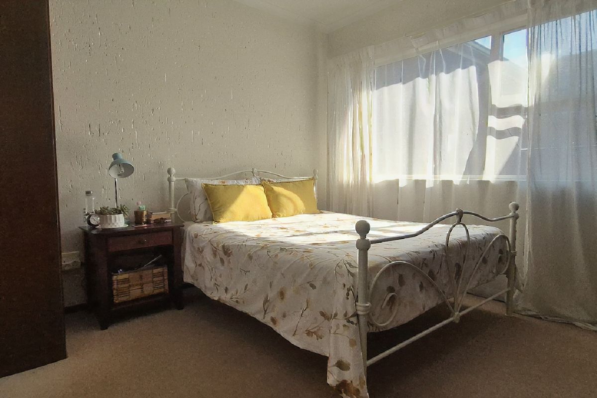 A sunlit bedroom featuring a built-in wardrobe, carpeted flooring, and large windows with natural light.