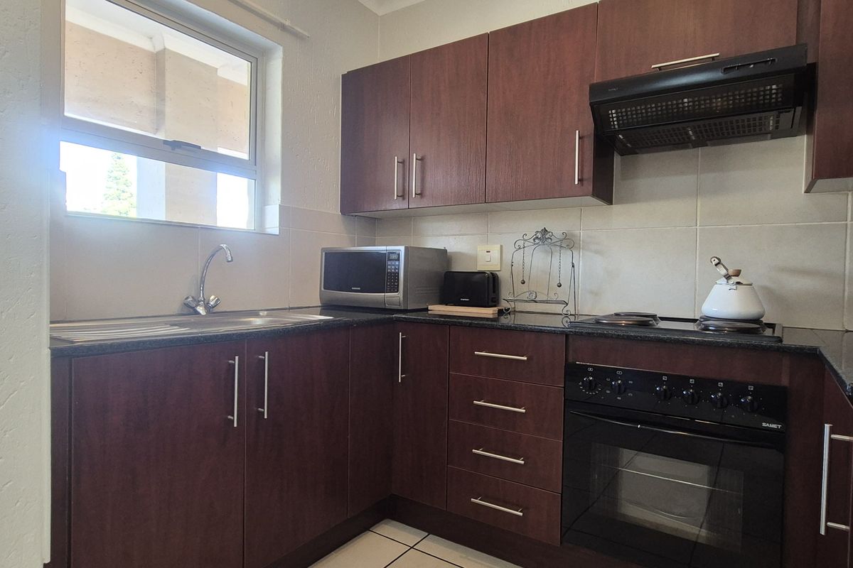 A functional kitchen featuring dark wood cabinetry, granite countertops, a built-in oven, hob, and extractor fan with tiled splashbacks.