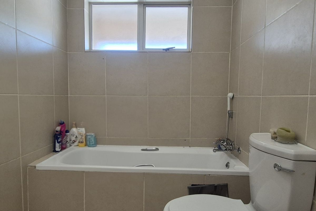 A functional bathroom featuring a built-in bathtub with shower mixer, a standard toilet, and neutral wall tiling throughout.