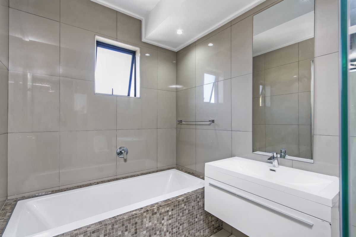 Modern bathroom featuring a built-in bathtub with mosaic tile surround, a wall-mounted vanity with integrated basin, and large format wall tiles.