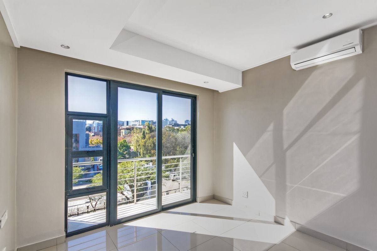 A bright, modern bedroom featuring tiled flooring, recessed ceiling lighting, a wall-mounted air conditioning unit, and large sliding glass doors leading to a balcony.
