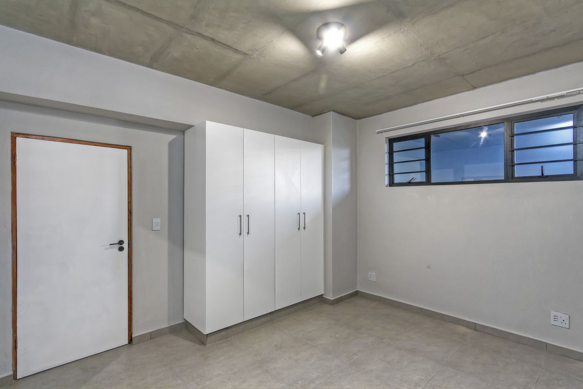 A clean, modern bedroom featuring a raw concrete ceiling, tiled flooring, and built-in white cabinetry.