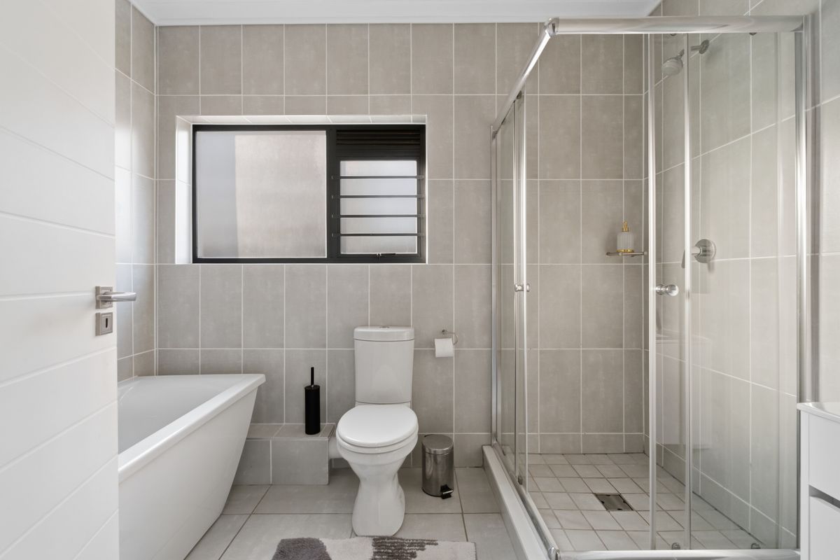 A modern, well-maintained bathroom featuring a separate glass-enclosed shower, a bathtub, and neutral floor-to-ceiling tiling.