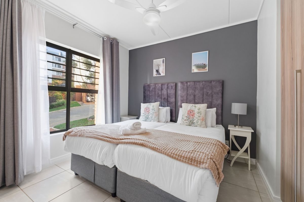 A well-maintained bedroom featuring tiled flooring, a ceiling fan, and a large window with views of the complex grounds.