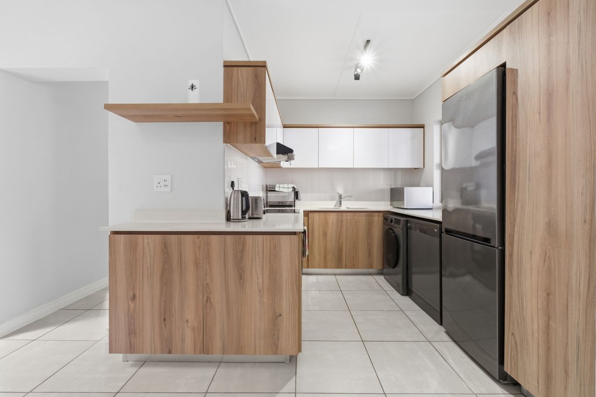 Modern kitchen featuring wood-grain cabinetry, white countertops, tiled flooring, and integrated appliance spaces, offering a clean and functional culinary environment.