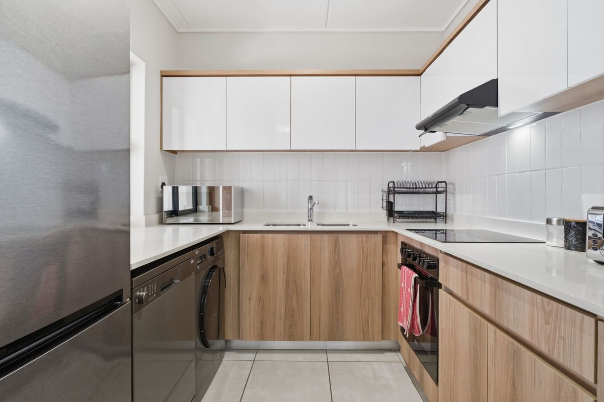 Modern kitchen featuring wood-grain cabinetry, white stone countertops, subway tile backsplash, integrated oven, hob, and extractor fan.