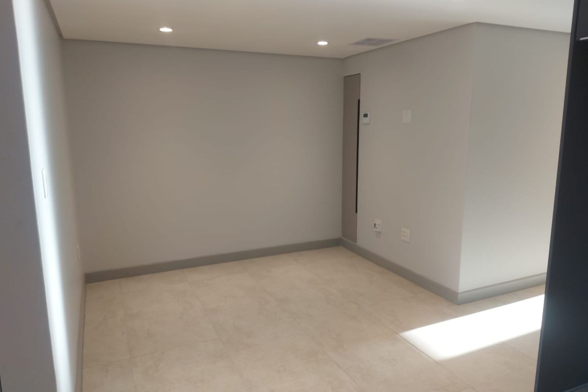 A bright, empty living area featuring neutral tiled flooring, recessed ceiling lighting, and clean, modern wall finishes.