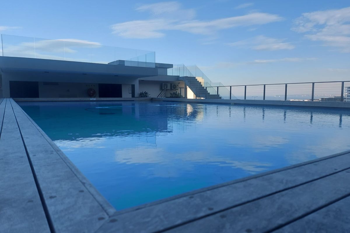 A modern rooftop swimming pool featuring glass balustrades, timber decking, and expansive views, providing a premium outdoor leisure space for residents.