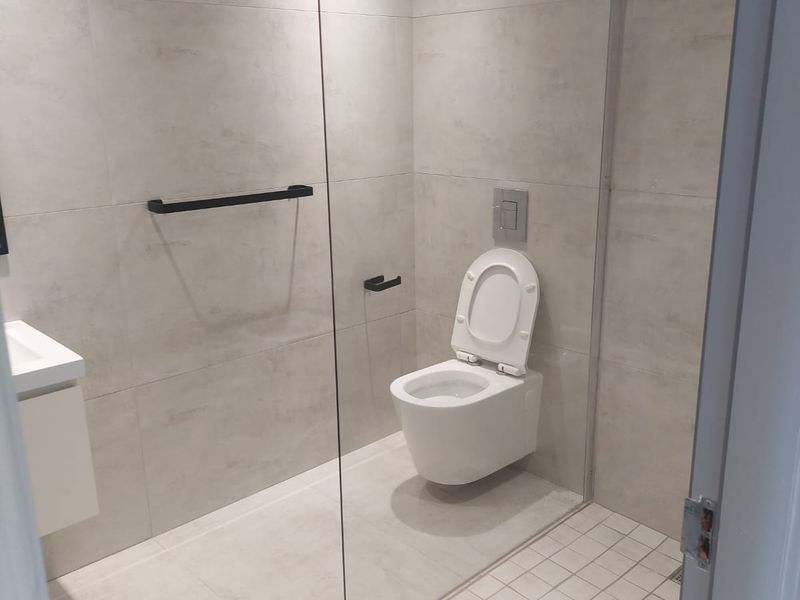 Modern bathroom featuring a walk-in shower with glass partition, wall-mounted toilet, and contemporary grey tiling throughout.