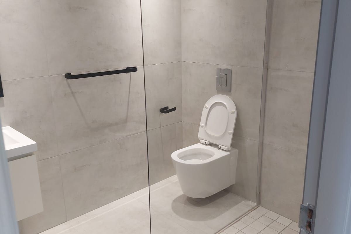 Modern bathroom featuring a walk-in shower with glass partition, wall-mounted toilet, and contemporary grey tiling throughout.
