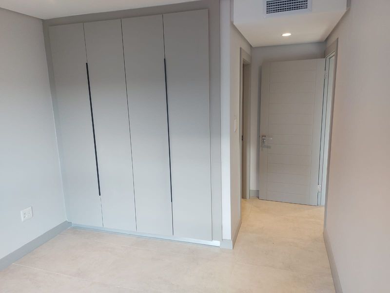 A modern bedroom featuring built-in floor-to-ceiling cabinetry, neutral tiled flooring, and recessed ceiling lighting.