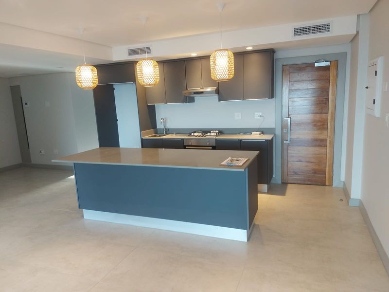 Modern open-plan kitchen featuring dark cabinetry, a central island with stone countertop, built-in gas hob, extractor fan, and integrated ducted air conditioning.