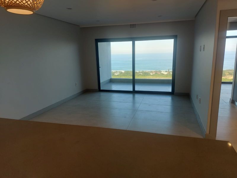 An open-plan living area featuring large sliding glass doors that open onto a balcony with expansive ocean views.