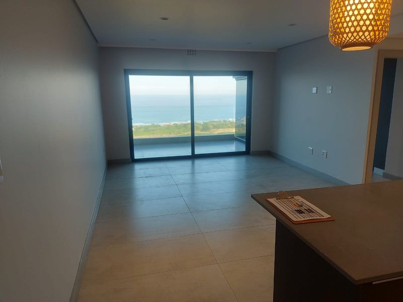 Open plan living area featuring large sliding glass doors that open to a balcony with expansive ocean views.