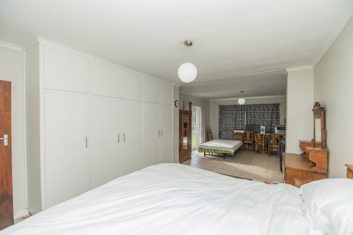 Spacious bedroom featuring extensive built-in floor-to-ceiling wardrobes and an adjoining study or seating area with direct access to the exterior.