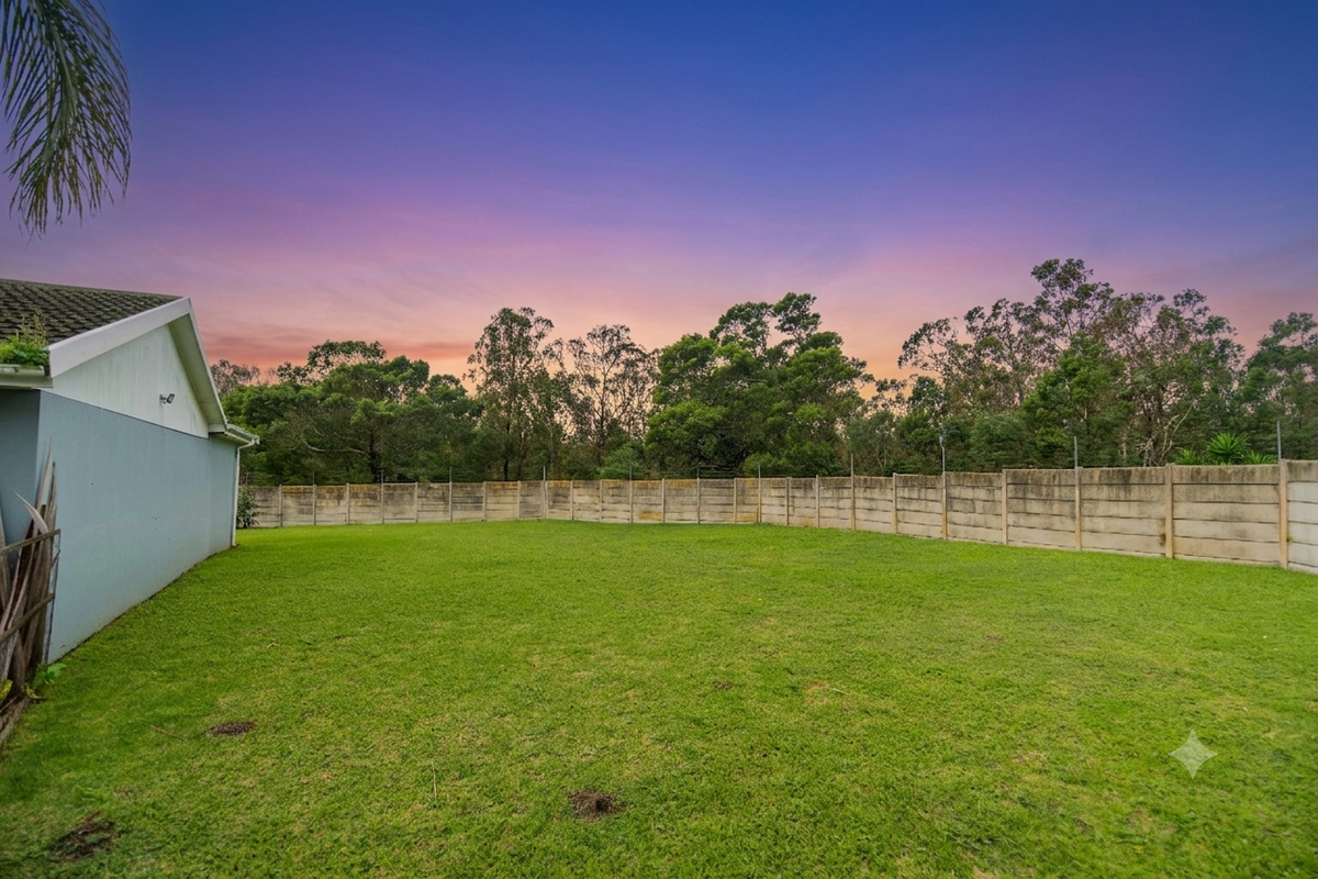 A spacious rear garden featuring a large lawn area enclosed by a concrete boundary wall, set against a scenic sunset backdrop.