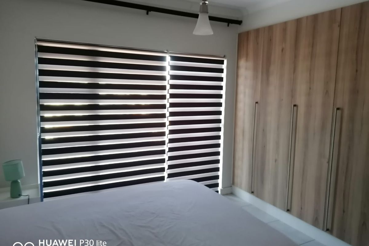 A well-maintained bedroom featuring built-in wooden wardrobes and modern zebra-style roller blinds.