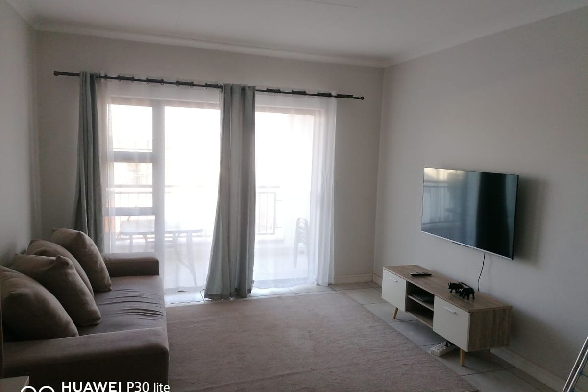 A bright living room featuring tiled flooring, neutral walls, and a sliding glass door providing access to an attached balcony.