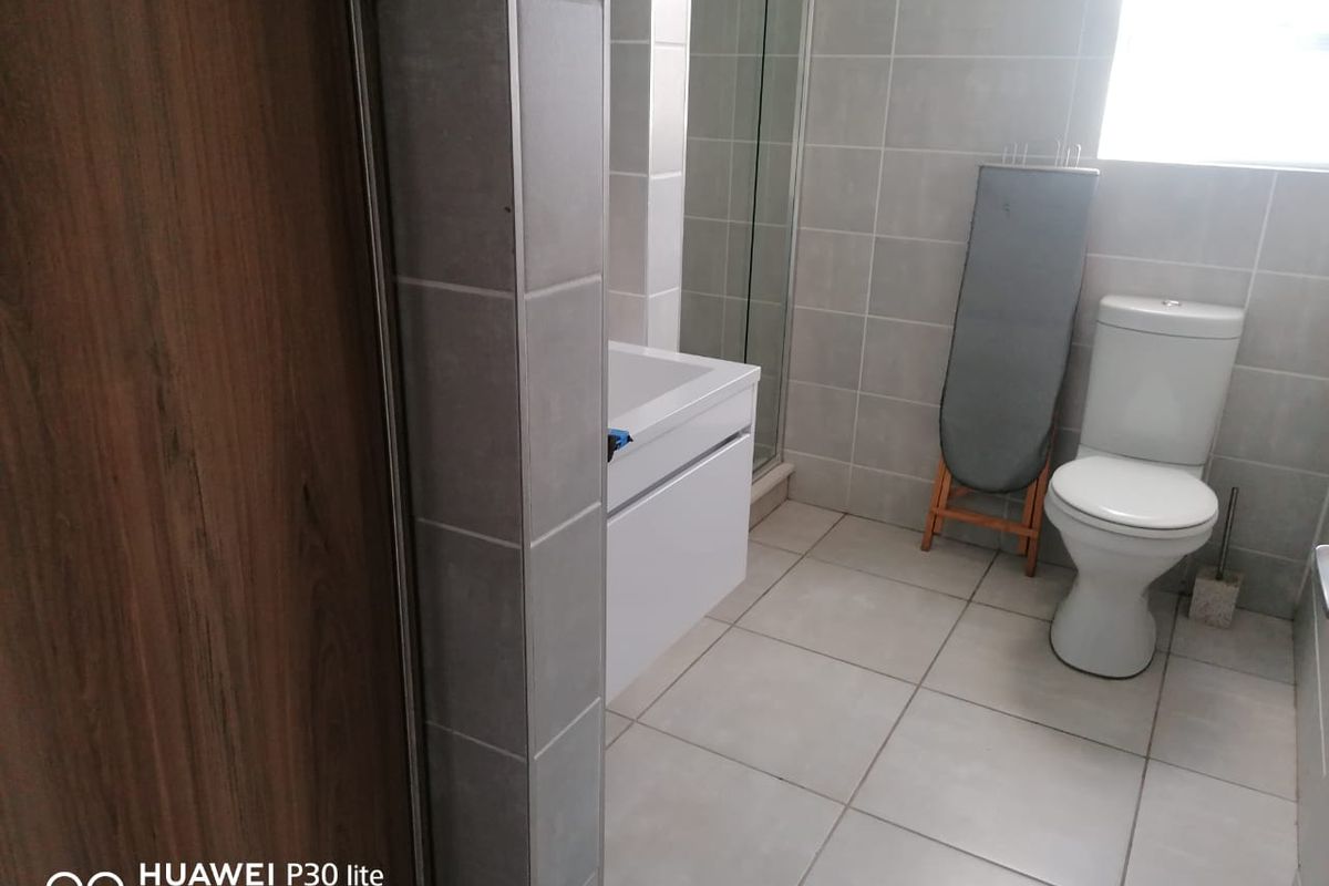 A modern bathroom featuring neutral wall and floor tiling, a glass-enclosed shower, and a white vanity unit.