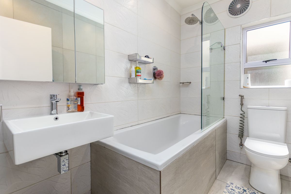 Modern bathroom featuring a wall-mounted basin, a bathtub with a glass shower screen, and a dual-flush toilet with tiled finishes.