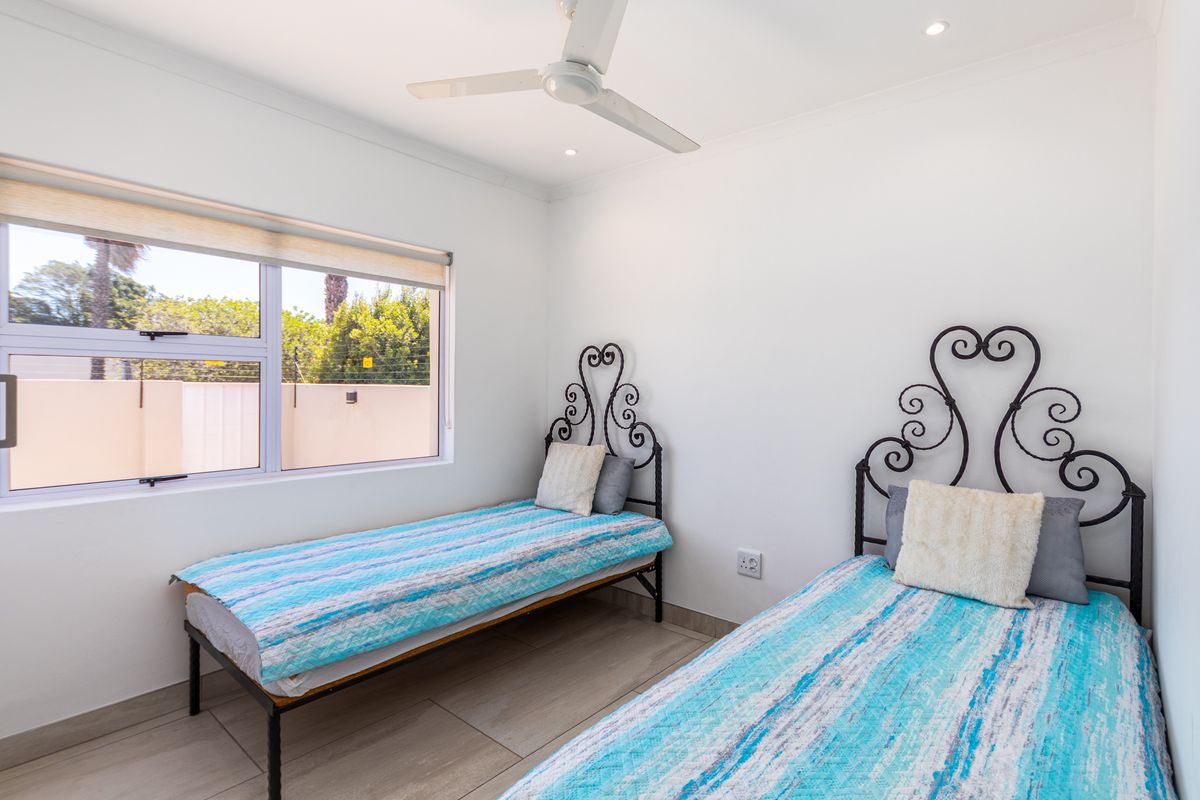 A bright bedroom featuring tiled flooring, a ceiling fan, and large windows providing natural light.
