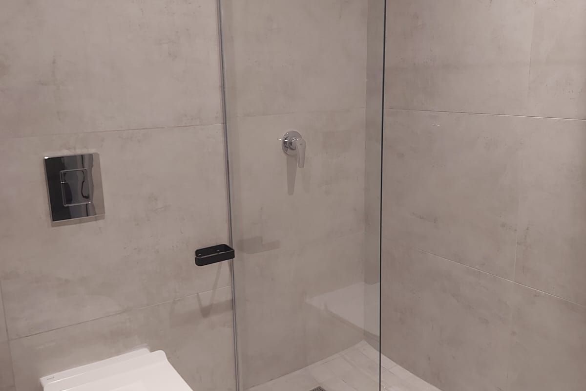 Modern bathroom featuring a wall-mounted toilet, a glass-enclosed walk-in shower with a rainfall showerhead, and neutral large-format wall tiles.