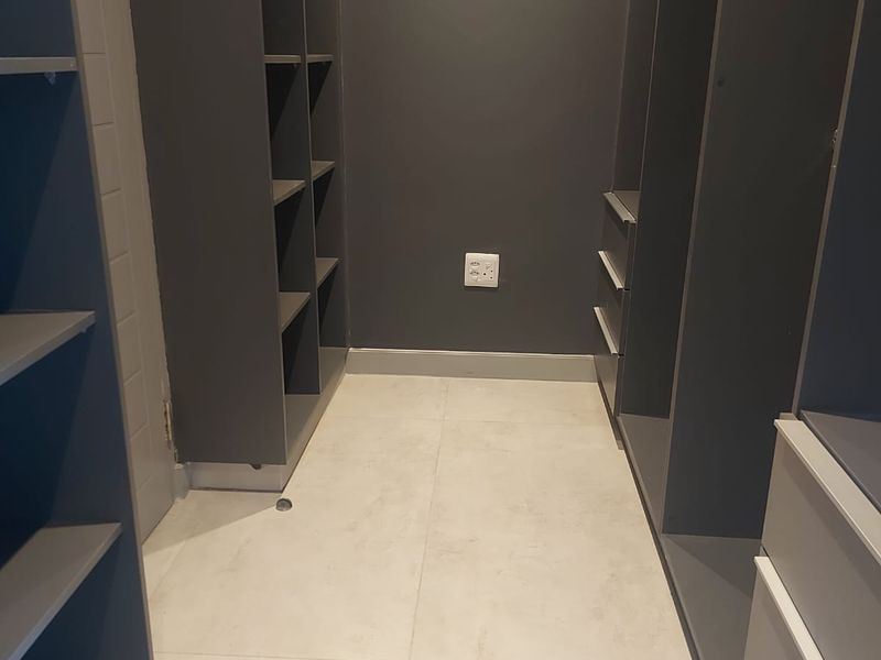 A walk-in closet featuring dark grey built-in cabinetry with open shelving and drawers, complemented by light-toned floor tiles.