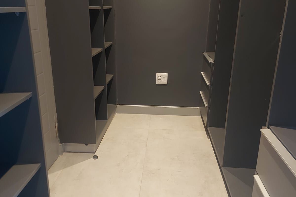 A walk-in closet featuring dark grey built-in cabinetry with open shelving and drawers, complemented by light-toned floor tiles.