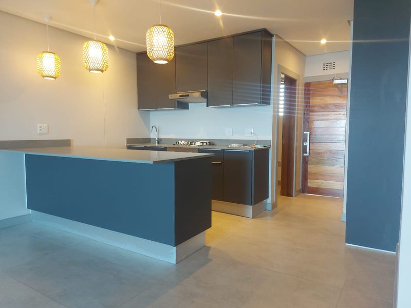 Modern open-plan kitchen featuring dark cabinetry, stone countertops, a built-in hob, and an extractor fan, seamlessly integrated with the living area.