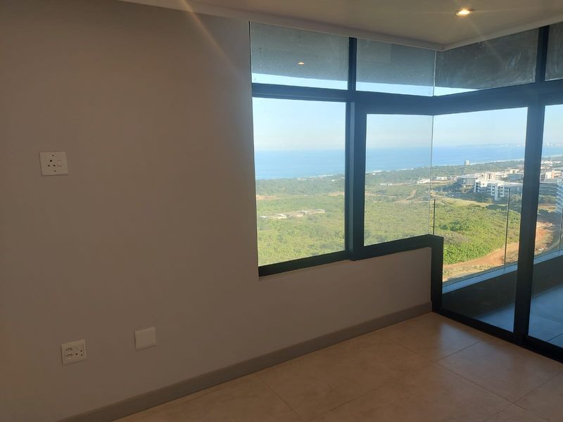 A bright, modern living area featuring floor-to-ceiling windows with expansive coastal and landscape views, tiled flooring, and recessed downlighting.